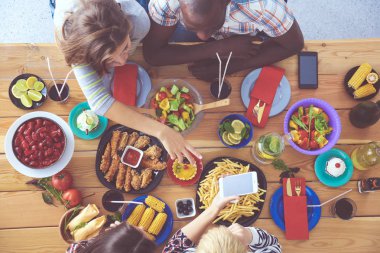 Ahşap masada otururken birlikte yemek yiyen bir grup insanın üst düzey görüntüsü. Masada yemek var. İnsanlar fast food yiyor..