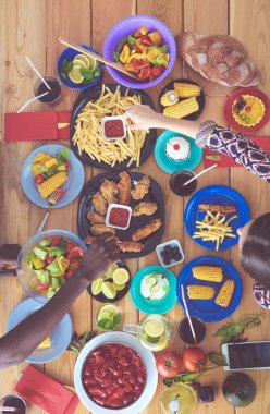 Ahşap masada otururken birlikte yemek yiyen bir grup insanın üst düzey görüntüsü. Masada yemek var. İnsanlar fast food yiyor..