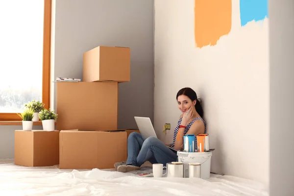 Ritratto di giovane donna mentre dipinge un nuovo appartamento, seduta con computer portatile. Giovane donna con computer portatile — Foto Stock