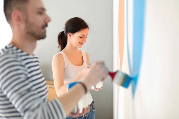 Retrato de feliz casal sorrindo jovem pintura parede interior da nova casa. jovem casal — Fotografia de Stock