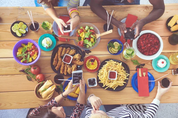 Vista superior do grupo de pessoas que jantam juntas enquanto estão sentadas à mesa de madeira. Comida na mesa. As pessoas comem fast food. — Fotografia de Stock