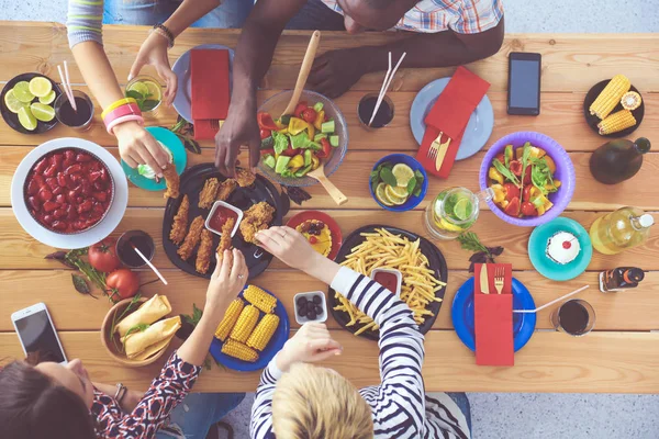 Vista superior del grupo de personas cenando juntas mientras están sentadas en la mesa de madera. Comida en la mesa. La gente come comida rápida. — Foto de Stock