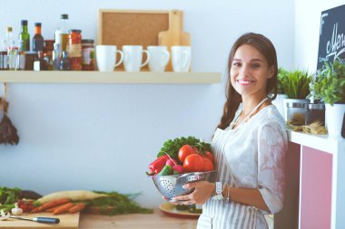 Mutfakta elinde sebzelerle gülümseyen genç bir kadın. Gülümseyen genç kadın