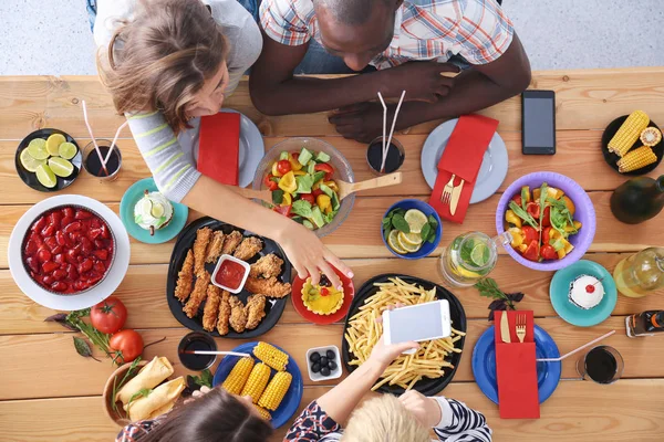 Vista superior do grupo de pessoas que jantam juntas enquanto estão sentadas à mesa de madeira. Comida na mesa. As pessoas comem fast food. — Fotografia de Stock