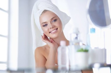 Güzel genç bir kadın yüzüne dokunuyor ve aynaya bakarken gülümsüyor.