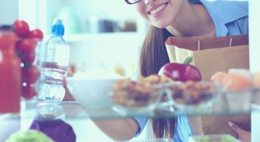 Sağlıklı yiyecek, sebze ve meyvelerle dolu açık buzdolabının yanında duran kadın portresi. Kadın portresi