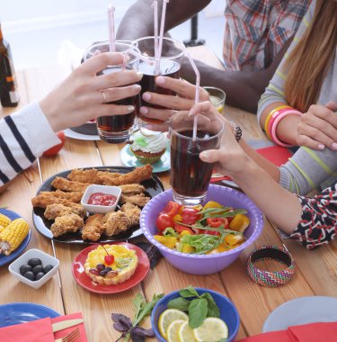 Ahşap masada otururken birlikte yemek yiyen bir grup insanın üst düzey görüntüsü. Masada yemek var. İnsanlar fast food yiyor..