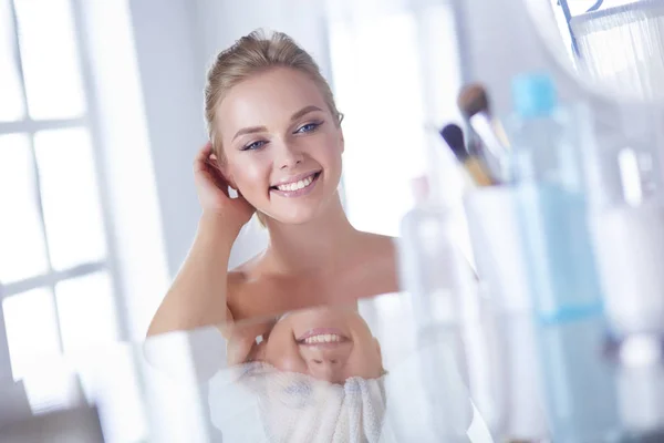 Joven hermosa mujer haciendo maquillaje cerca del espejo, sentado en el escritorio — Foto de Stock