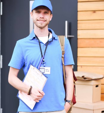 Mavi üniformalı gülümseyen kurye servis konseptine paket kutusu teslim eden teslimatçı.