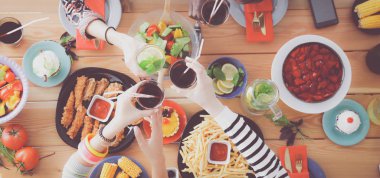 Ahşap masada otururken birlikte yemek yiyen bir grup insanın üst düzey görüntüsü. Masada yemek var. İnsanlar fast food yiyor..