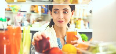 Sağlıklı yiyecek, sebze ve meyvelerle dolu açık buzdolabının yanında duran kadın portresi.