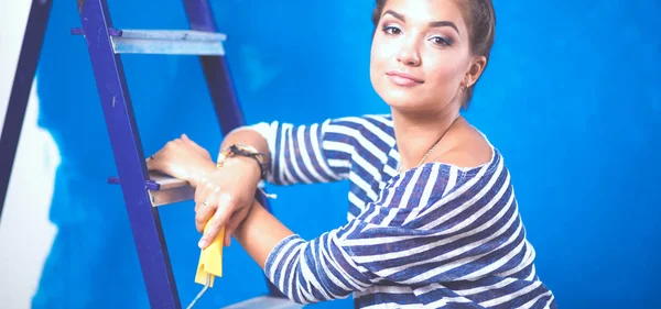 Beautiful young woman doing wall painting, standing on ladder. Beautiful young woman — Stock Photo, Image