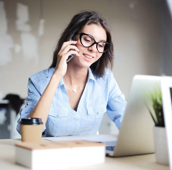 Mooie jonge zakenvrouw die aan het bureau zit en met haar mobiel praat. Zakelijke vrouw — Stockfoto