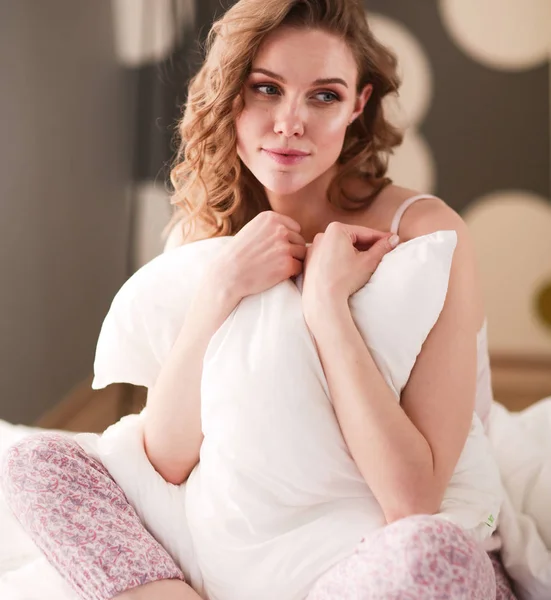 Mujer joven sosteniendo una almohada mientras está sentada en su cama —  Fotos de Stock