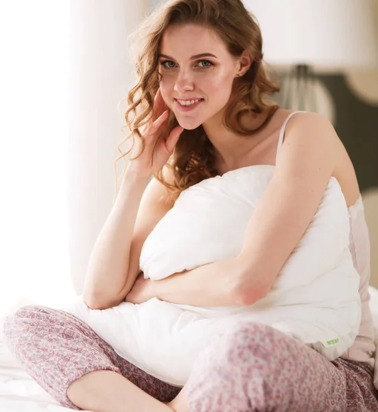 Young woman holding a pillow while sitting on her bed. — Stock Photo, Image