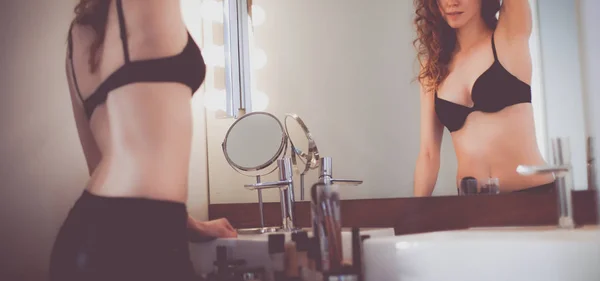 Молодая женщина смотрит на себя в зеркало в ванной комнате . — стоковое фото