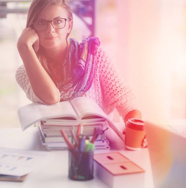 Kitapların arasında bir masada oturan genç bir kadın. Öğrenci