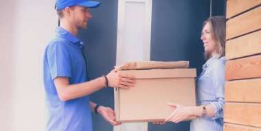 Mavi üniformalı gülümseyen kurye servis konseptine paket kutusu teslim eden teslimatçı.
