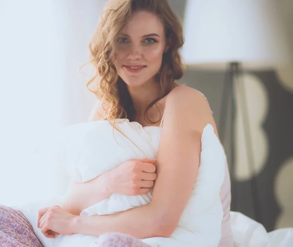 Junge Frau hält ein Kissen während sie auf ihrem Bett sitzt. — Stockfoto