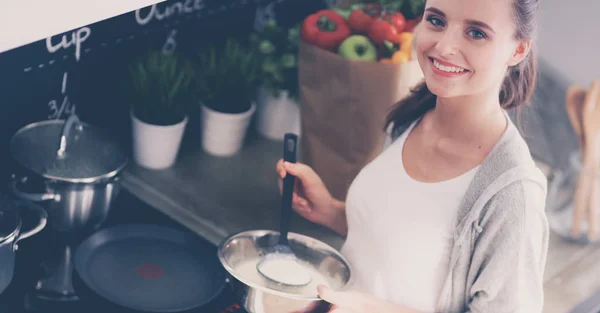 Mujer joven cocinando panqueques en la cocina de pie cerca de la estufa — Foto de Stock