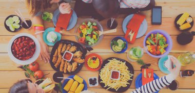 Ahşap masada otururken birlikte yemek yiyen bir grup insanın üst düzey görüntüsü. Masada yemek var. İnsanlar fast food yiyor..