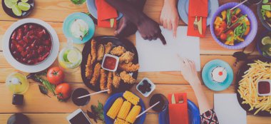 Ahşap masada otururken birlikte yemek yiyen bir grup insanın üst düzey görüntüsü. Masada yemek var. İnsanlar fast food yiyor..
