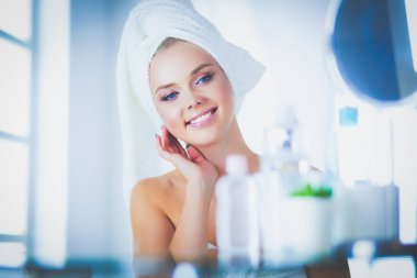 Güzel genç bir kadın yüzüne dokunuyor ve aynaya bakarken gülümsüyor.