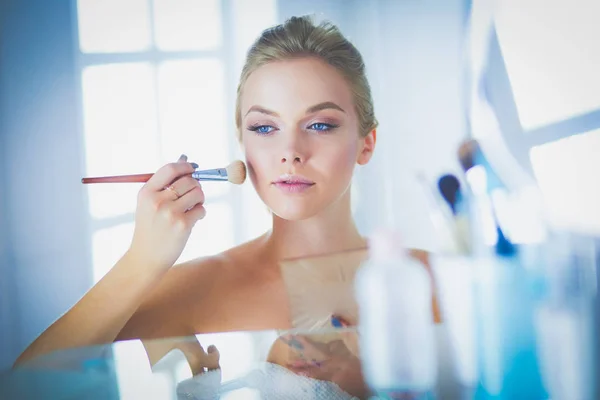 Joven hermosa mujer haciendo maquillaje cerca del espejo, sentado en el escritorio — Foto de Stock