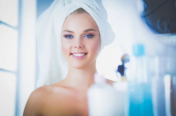Hermosa joven mujer está tocando su cara y sonriendo mientras se mira al espejo — Foto de Stock