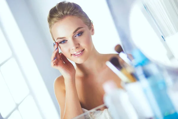 Junge schöne Frau schminkt sich in der Nähe des Spiegels und sitzt am Schreibtisch Stockbild