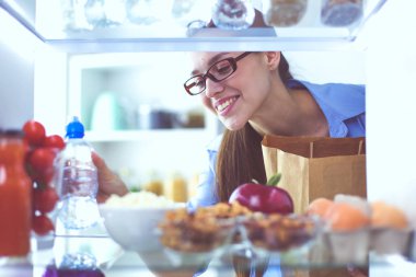 Sağlıklı yiyecek, sebze ve meyvelerle dolu açık buzdolabının yanında duran kadın portresi..