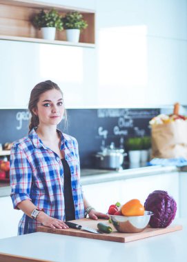 Masanın yanındaki mutfakta sebze doğrayan genç bir kadın..