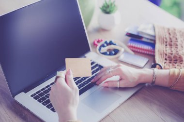 Kredi kartı tutan ve dizüstü bilgisayar kullanan genç bir kadın. Çevrimiçi alışveriş kavramı