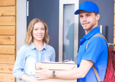 Mavi üniformalı gülümseyen kurye servis konseptine paket kutusu teslim eden teslimatçı. Mavi üniformalı gülümseyen teslimatçı.
