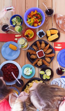 Ahşap masada otururken birlikte yemek yiyen bir grup insanın üst düzey görüntüsü. Masada yemek var. İnsanlar fast food yiyor..