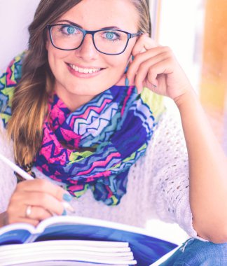 Kitapların arasında bir masada oturan genç bir kadın. Öğrenci