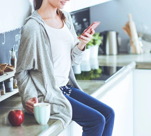 Frau sitzt mit Handy in moderner Küche. — Stockfoto