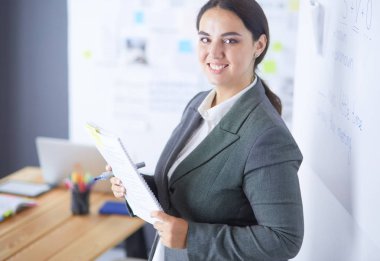 Ayakta ve ofiste bir kitap tutan genç gülümseyen kadın