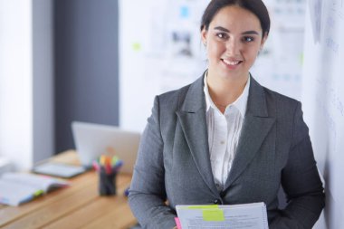 Ayakta ve ofiste bir kitap tutan genç gülümseyen kadın