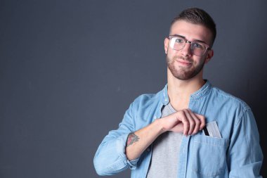 Gri arka planda duran bir kredi kartı tutan genç adam. Genç girişimci..