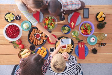 Ahşap masada otururken birlikte yemek yiyen bir grup insanın üst düzey görüntüsü. Masada yemek var. İnsanlar fast food yiyor..