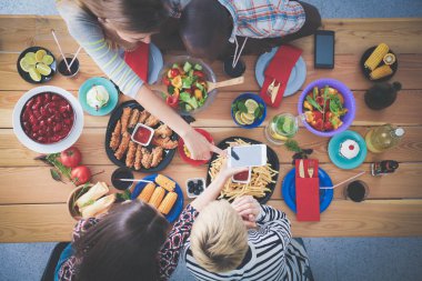Ahşap masada otururken birlikte yemek yiyen bir grup insanın üst düzey görüntüsü. Masada yemek var. İnsanlar fast food yiyor..