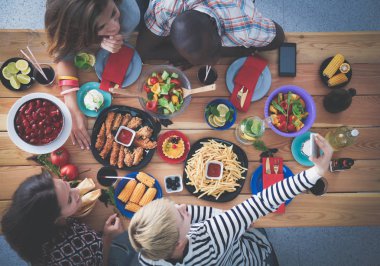 Ahşap masada otururken birlikte yemek yiyen bir grup insanın üst düzey görüntüsü. Masada yemek var. İnsanlar fast food yiyor..