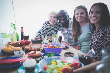Ahşap masada otururken birlikte yemek yiyen bir grup insanın üst düzey görüntüsü. Masada yemek var. İnsanlar fast food yiyor..