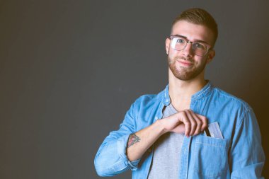 Gri arka planda duran bir kredi kartı tutan genç adam. Genç girişimci..