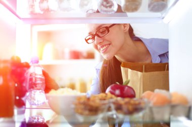 Sağlıklı yiyecek, sebze ve meyvelerle dolu açık buzdolabının yanında duran kadın portresi..
