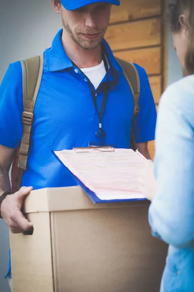 Homem de entrega sorridente em uniforme azul entregando caixa de encomendas ao destinatário conceito de serviço de correio. Sorrindo homem de entrega em uniforme azul — Fotografia de Stock