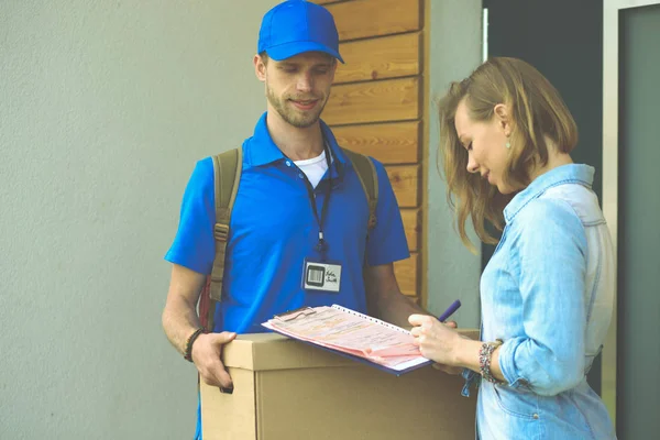 Repartidor sonriente con uniforme azul que entrega la caja de paquetes al destinatario: concepto de servicio de mensajería. Repartidor sonriente en uniforme azul — Foto de Stock