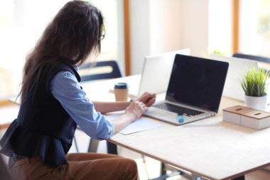 Ofis masasında dizüstü bilgisayarla oturan genç bir kadın. Genç bir kadın. Dizüstü bilgisayar