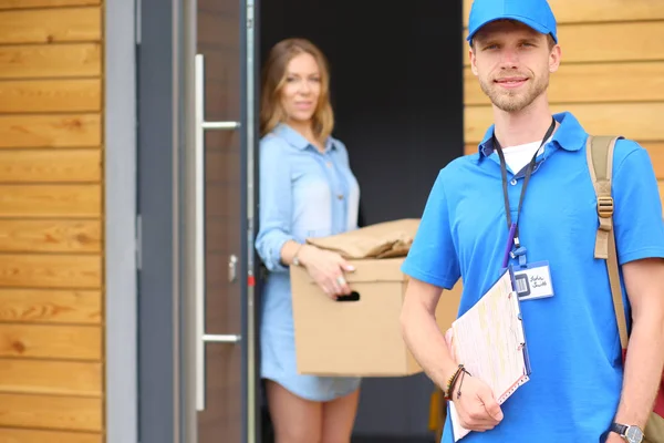 Repartidor sonriente con uniforme azul que entrega la caja de paquetes al destinatario: concepto de servicio de mensajería. Repartidor sonriente en uniforme azul —  Fotos de Stock